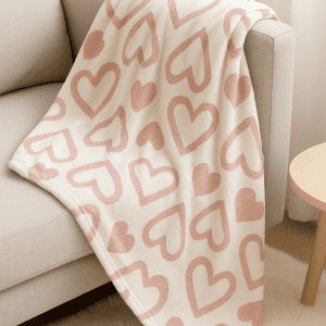 "Velvet Heart Blanket – Folded white plush throw with shiny pink hearts placed in a woven basket. Cozy and decorative storage idea.